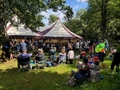 A crowd gathered outside a tent on a sunny patch of grass.