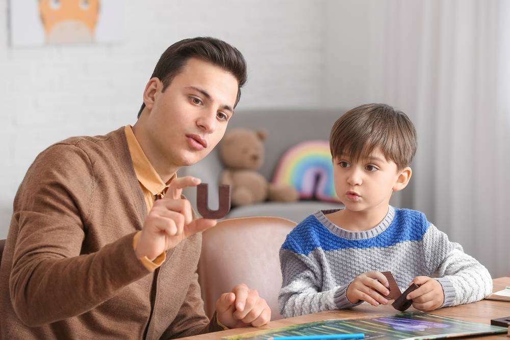 Practitioner with young patient in session, holding the letter 'U'.
